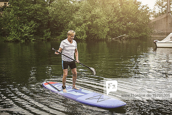 Paddelboarden eines älteren Mannes in voller Länge auf See während eines SUP-Kurses