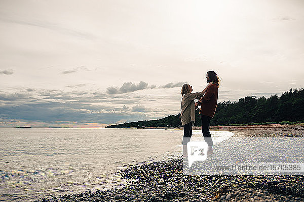 Paar in voller Länge am Meeresufer am Strand gegen den Himmel stehend