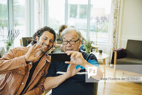 Videokonferenz zwischen einem älteren Mann und seinem Enkel mit einem Smartphone im Altenpflegeheim