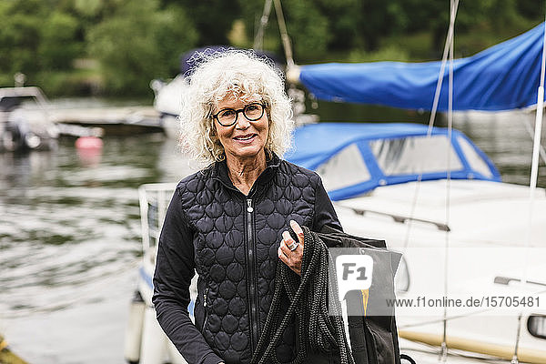 Porträt einer selbstbewussten älteren Frau  die während des Bootsführerkurses Schwimmweste und Seil in der Hand hält