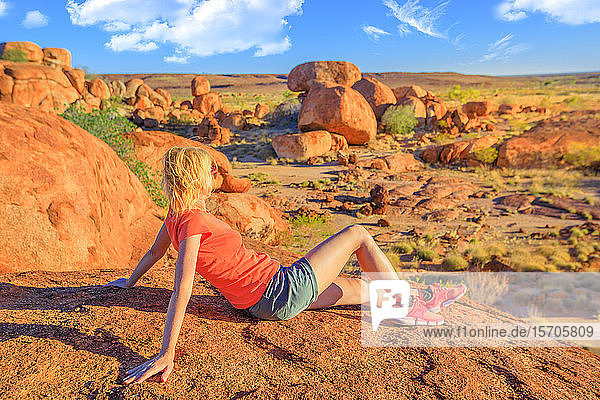 Touristin auf dem Nyanjiki Lookout bei Sonnenuntergang  die den Panoramablick und die leuchtenden Farben der gigantischen Felsblöcke der natürlichen Felsformationen bei Karlu Karlu (Devils Marbles)  Northern Territory  Australien  Pazifik  bewundert