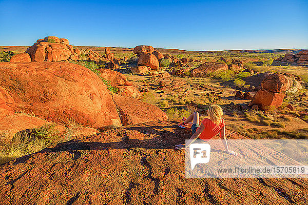 Touristin auf dem Gipfel des Karlu Karlu (Devils Marbles) Conservation Reserve mit Blick auf ein Panorama aus Granitblöcken und Felsformationen bei Sonnenuntergang  Outback  Northern Territory  Australien  Pazifik