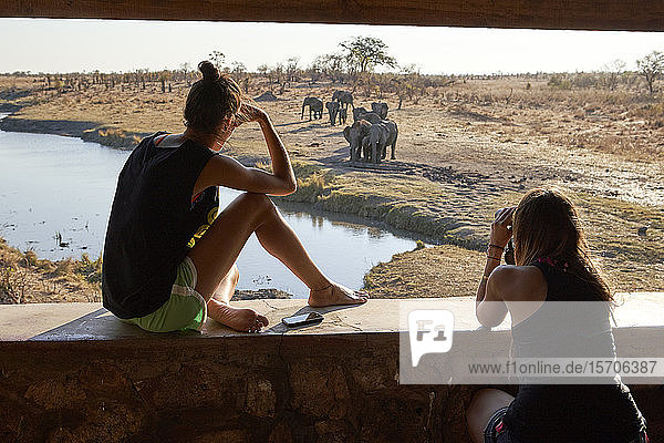 Zwei Frauen beobachten eine Elefantenherde im Fluss von einem Aussichtspunkt aus  Hwange-Nationalpark  Simbabwe