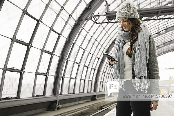 Glückliche junge Frau mit Smartphone auf dem Bahnsteig  Berlin  Deutschland