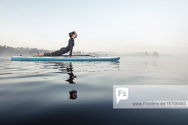 Frau praktiziert morgens Paddelbrett-Yoga auf dem Kirchsee  Bad Tölz  Bayern  Deutschland