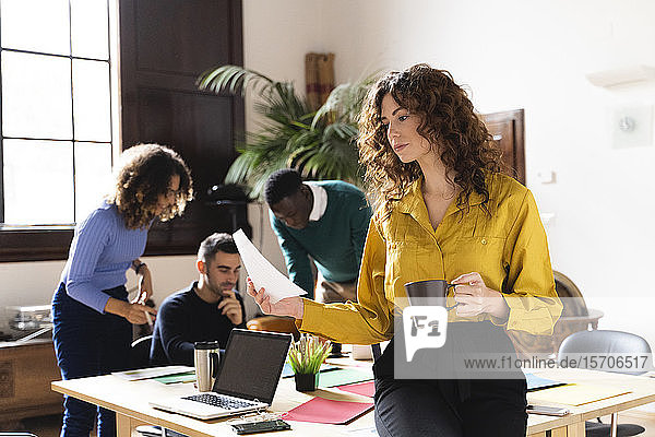 Woman with paper and coffee cup in office with colleagues in background