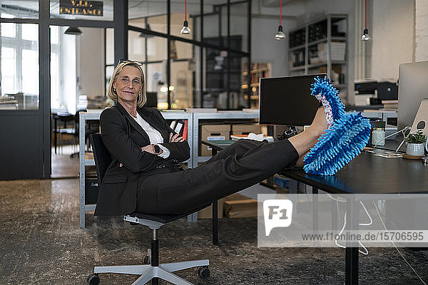 Reife Geschäftsfrau mit Füßen auf dem Schreibtisch  die im Büro Reinigungsschuhe trägt