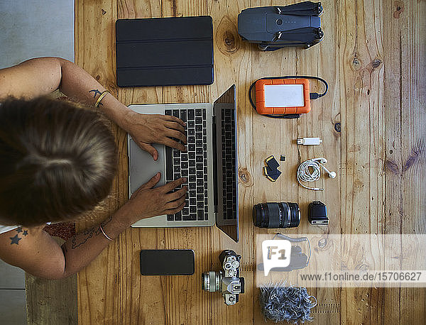 Person sitting at table with photografic equipment using laptop overhead view