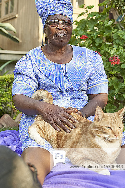 Ältere Frau mit einer Katze  die auf einer Decke im Garten sitzt