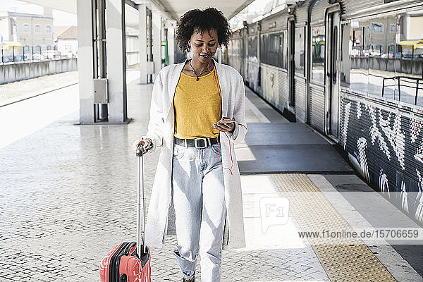 Lächelnde junge Frau mit Kopfhörern und Smartphone am Bahnsteig
