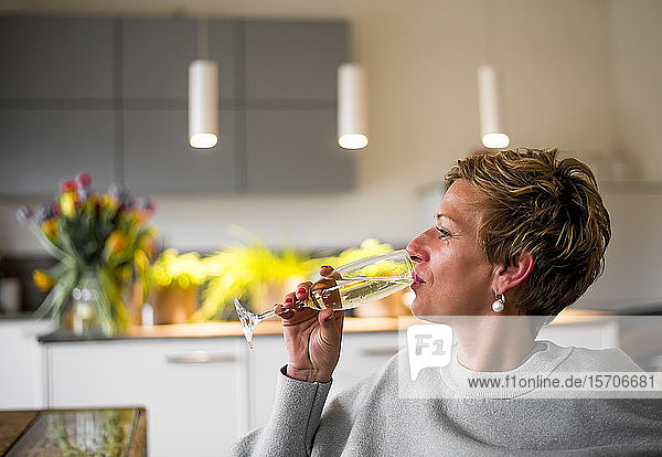 Frau trinkt ein Glas Champagner in der heimischen Küche