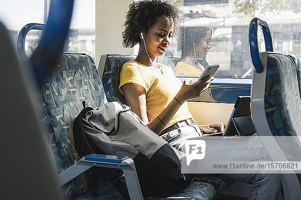 Junge Frau mit Kopfhörern mit Smartphone und Tablet im Zug