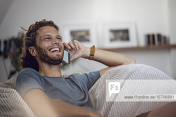 Laughing young man relaxing in beanbag at home talking on the phone