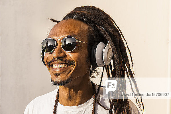 Porträt eines lächelnden reifen Mannes mit Dreadlocks und Kopfhörern, der Musik hört und zur Seite schaut