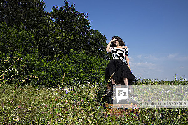Junge Frau sitzt auf einem Stapel alter Koffer auf einer Wiese