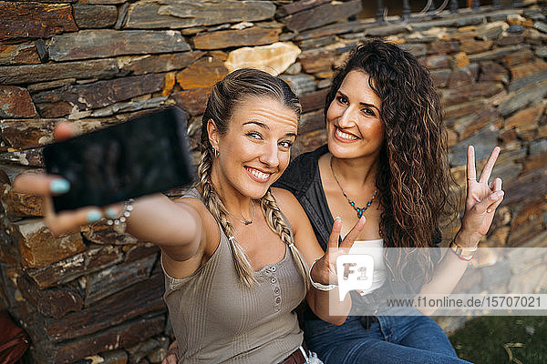 Zwei glückliche Frauen sitzen in einem Steinhaus und machen ein Selfie