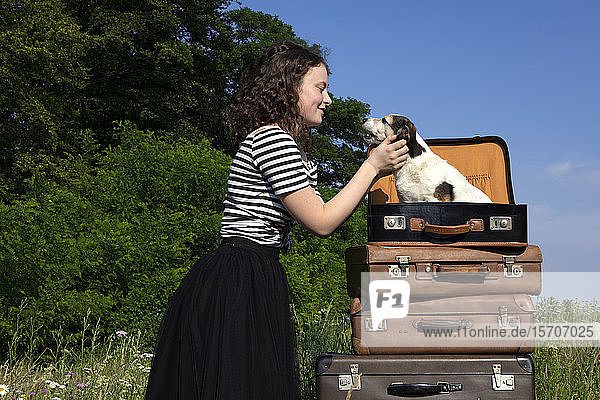 Junge Frau kuschelt kleinen Hund  der im Koffer sitzt