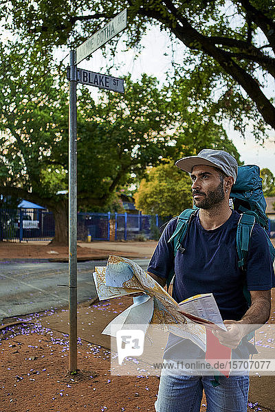 Rucksacktourist steht auf einer Straße und hält eine Karte