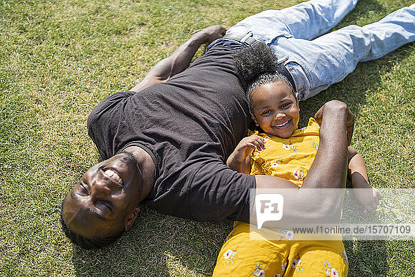 Happy father and daughter lying on a meadow in a park