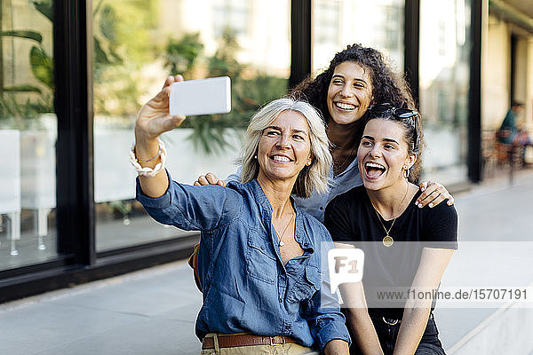 Three laughing women taking selfie in the city