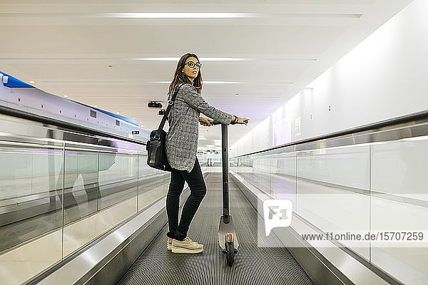 Businesswoman with her electric scooter on moving walkway