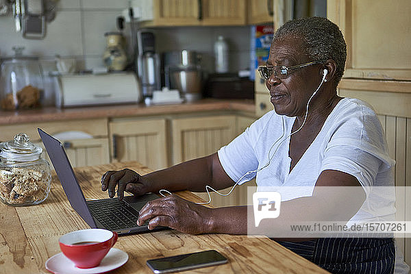 Ältere Frau sitzt mit Laptop am Küchentisch