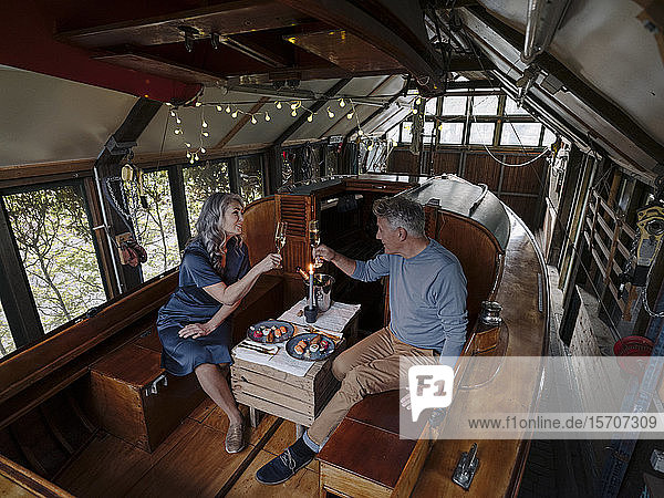 Senior couple having a candlelight dinner on a boat in boathouse clinking champagne glasses