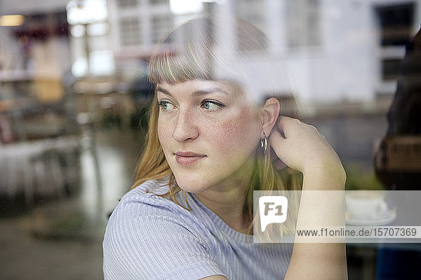 Porträt einer jungen Frau in einem Cafe  die aus dem Fenster schaut