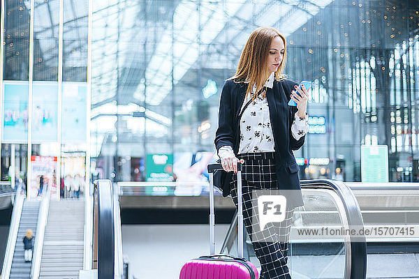 Junge Frau mit Koffer und Handy am Bahnhof