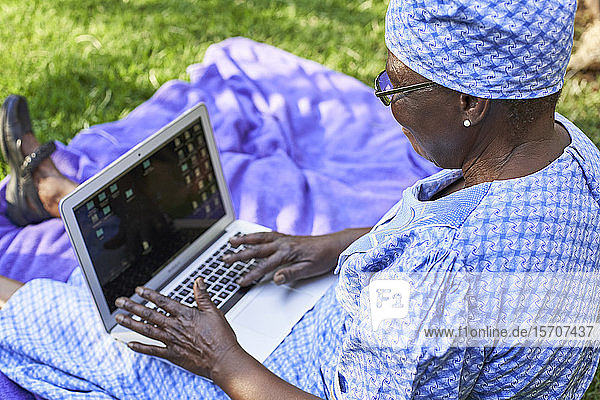 Ältere Frau sitzt mit Laptop auf dem Rasen