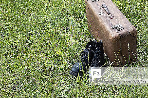 Old brown leather suitcase and pair of black boots on a meadow