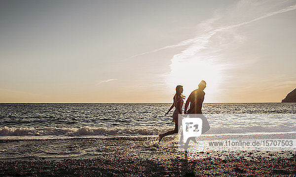 Junges Paar rennt bei Sonnenuntergang am Strand