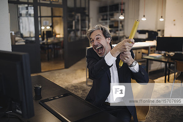 Angry senior businessman with giant pencil at desk in office