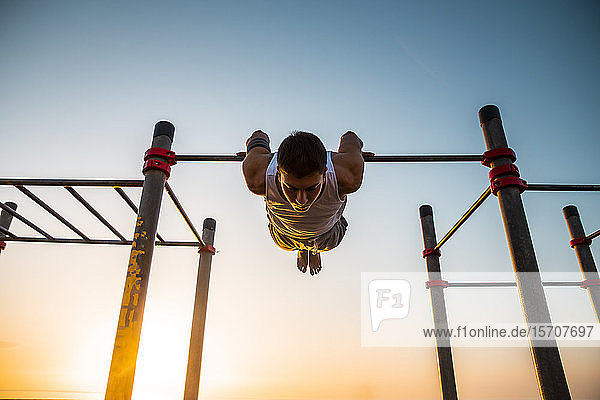 Junger Mann übt bei Sonnenaufgang Gymnastik in einer Turnhalle im Freien