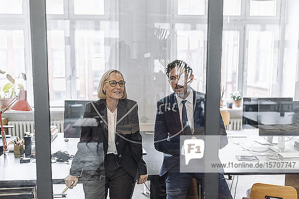 Businessman and businesswoman looking at drawing on glass pane in office