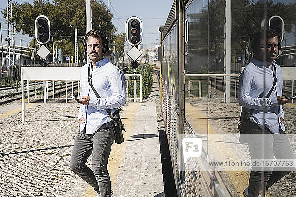 Junger Mann mit Kopfhörern und Smartphone verlässt den Zug