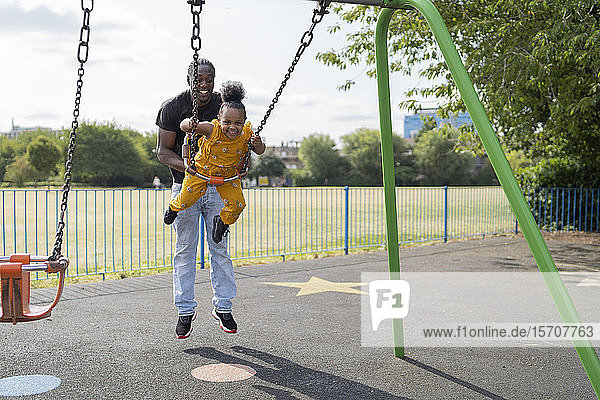 Father with happy daughter swinging on a playground