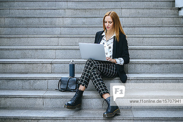 Junge Geschäftsfrau sitzt mit Laptop auf der Treppe