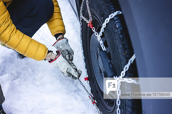 Mann legt die Schneeketten an sein Auto