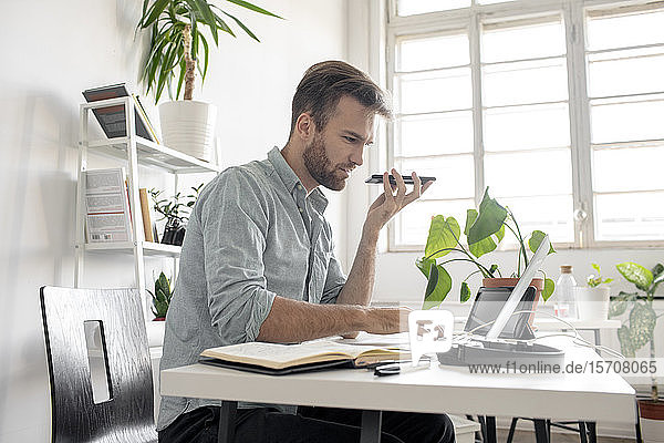 Mann benutzt Smartphone und Laptop am Schreibtisch im Büro