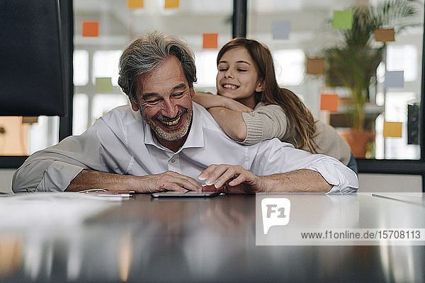 Happy senior buisinessman and girl looking at tablet in office