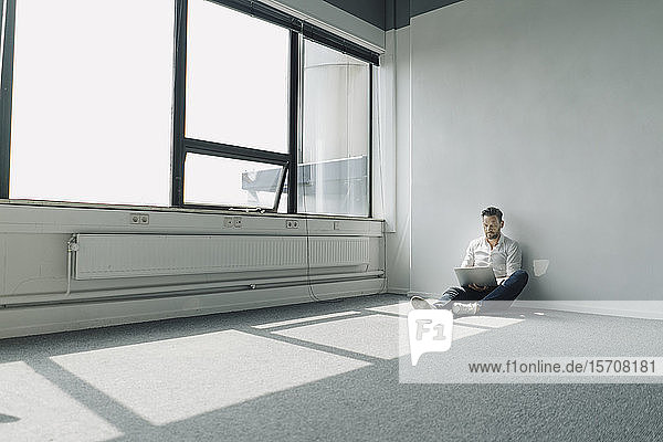 Mature businessman sitting on the floor in empty office using laptop