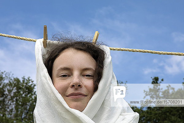 Porträt einer lächelnden jungen Frau  in weißes Tuch gewickelt  an der Wäscheleine hängend