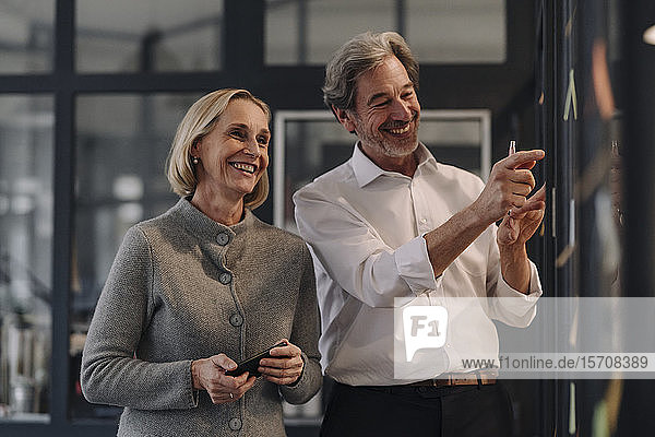 Happy businessman and businesswoman working on sticky notes at glass pane in office