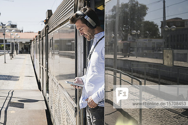 Young man with headphones and smartphone standing in train door