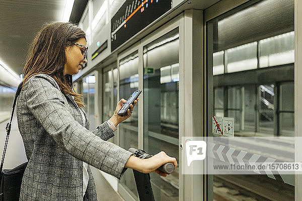 Junge Geschäftsfrau mit E-Scooter beim Telefonieren in der U-Bahn-Station