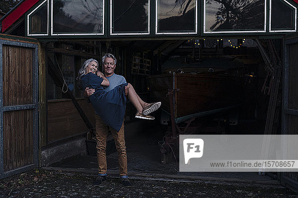 Senior man carrying his wife in front of boathouse
