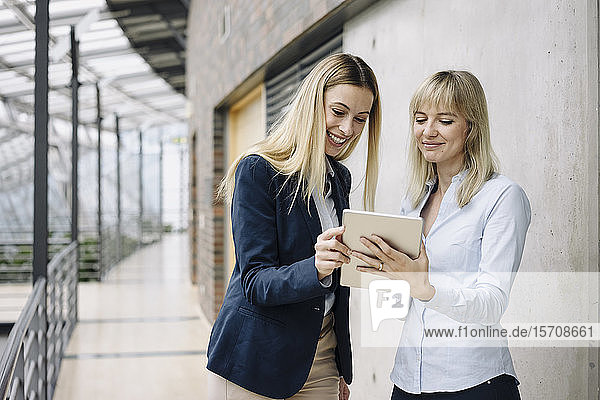 Two happy young businesswomen with tablet in modern office building