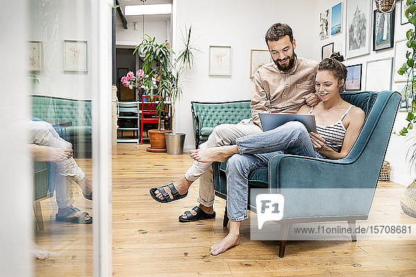 Junges Paar sitzt im Sessel und benutzt ein digitales Tablett
