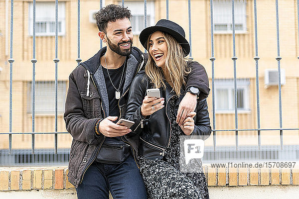 Portrait of laughing young couple with their mobile phones in the city